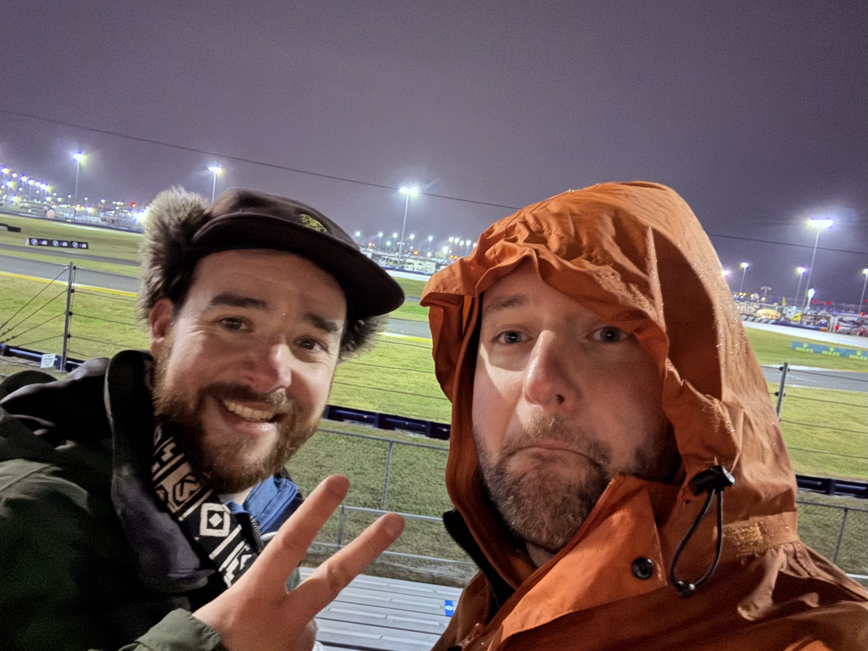 Two thirtysomething men in cold-weather rain gear by a race track at night